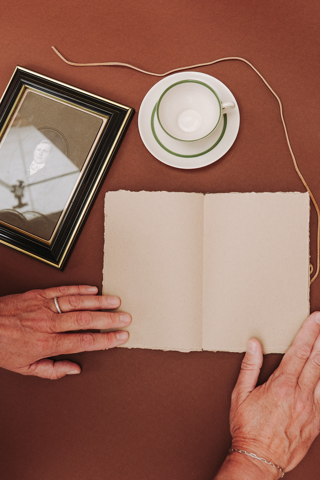 Open artist book with cream deckle-edge pages, vintage frame and teacup